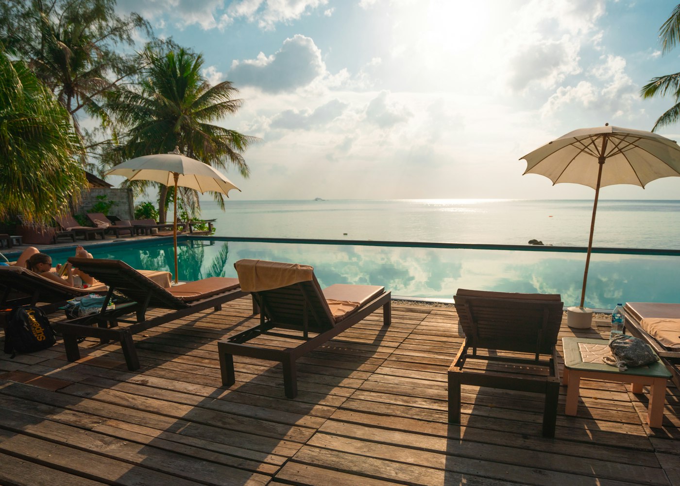 Piscina com deck de madeira e espreguiçadeiras entre coqueiros