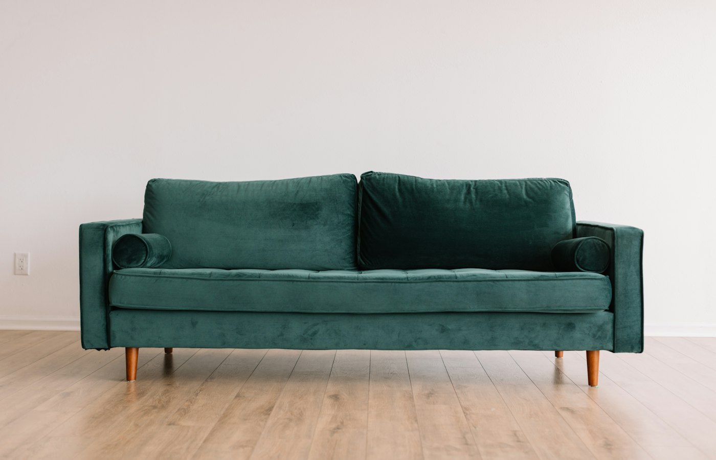 Sofá de veludo verde em uma sala clara com piso de madeira