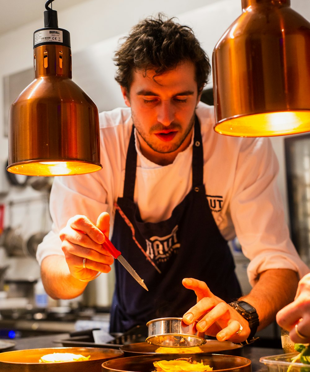 Cozinheiro finalizando um prato sob as luminárias da cozinha